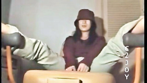 Asian woman in bucket hat and maroon top sits between spread gray pants legs teasing