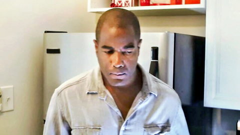 Bald black man in open shirt standing seriously in kitchen by fridge