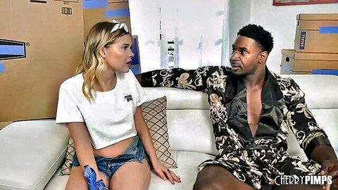 Blonde petite Coco Lovelock in white tee and shorts chats with Black man in silk robe