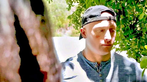Bald male performer in cap, intense gaze outdoors in Jennifer White Caged In