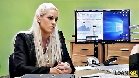 Sexy long-haired blonde MILF in tight black blazer sits at office desk with computer screens