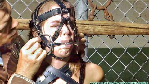 Bearded man grips bridle gag on drooling blonde slave's face, exposing her tits in leather harness bondage