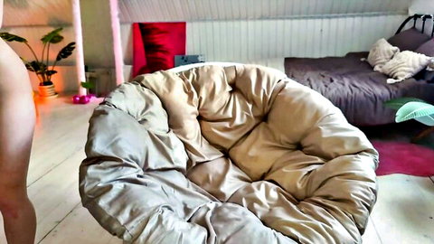 Nude woman's bare ass and legs visible beside large beige poof chair in cozy bedroom