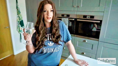 Busty MILF in casual Adidas tee holding wine glass in kitchen tease