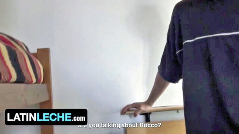Latino guy in tank top standing by bunk bed ladder in dorm room with latinleche watermark
