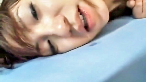 Cute young Asian girl with half-closed eyes and tongue out in ecstasy on blue bed