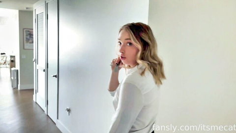 Sexy blonde babe in white top teasing over shoulder while whispering seductively on phone in hallway