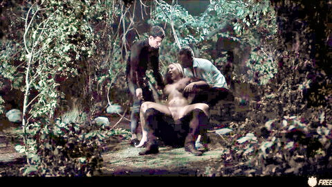 Muscular shirtless man exposed in woods with two suited guys in intense group scene