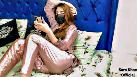 Sara Khan in sexy pink outfit, sitting on bed with phone and mask