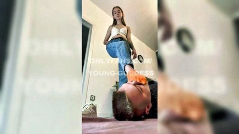 Young femdom mistress in jeans and sneakers tramples humiliated slave's face on floor