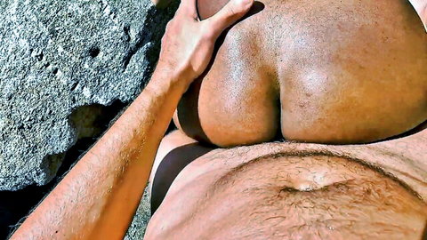 White hand groping massive bare ebony ass cheeks outdoors on rocky beach