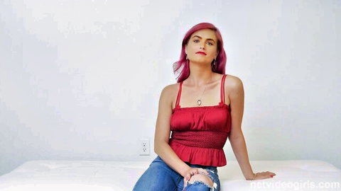Katrina with pink hair in red ruched top and ripped jeans, sitting and spreading legs