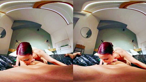 Redhead babe with perky tits sucking thick cock on black bed in modern bedroom.