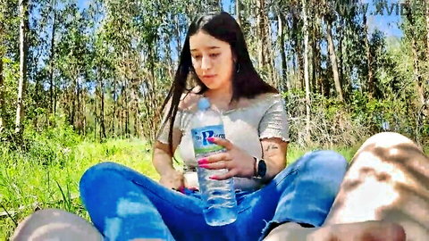 Brunette Latina babe in tank top and jeans sits in forest grass holding water bottle