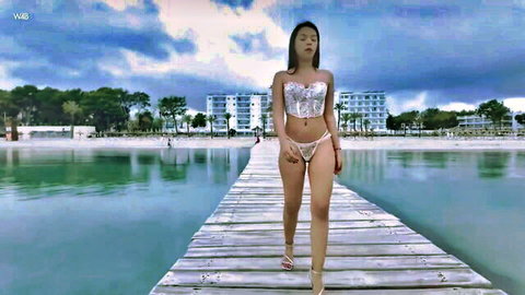 Sexy Asian babe in skimpy silver bikini struts on beach pier flaunting curves and tits outdoors
