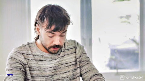 Handsome Caucasian man with shaggy hair and mustache in gray striped sweater looking thoughtful by window