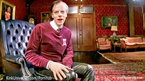 Man in maroon Kink University sweater sits talking in luxurious red velvet room