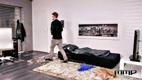 Redhead guy in gray pants walks into modern bedroom with messy black couch bed and scattered clothes
