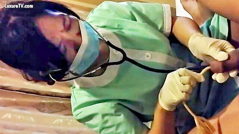 Asian nurse in green scrubs and mask examines patient's bare leg and foot with stethoscope