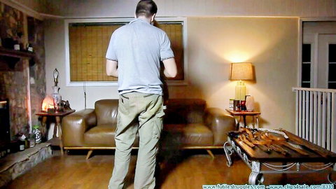 Clothed man stands back to camera in BDSM living room with wooden paddles on table for slave punishment