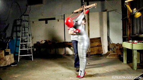Diamondly bound in silver tape mummification with arms suspended overhead in BDSM scene
