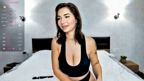 Sexy Latina webcam babe with huge tits smiling in low-cut tank top on bed