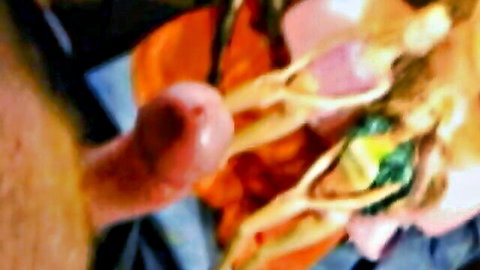Blurry close-up of erect penis amid colorful blonde doll figures in fetish lesbian session