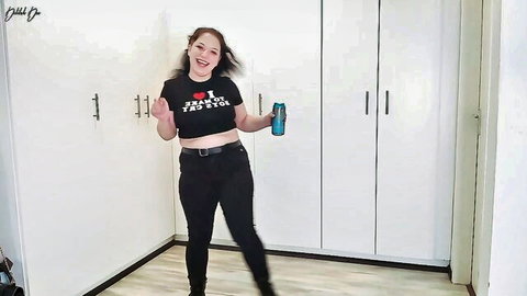 Smiling femdom mistress in tight black crop top 'I F MY JOB' and pants holding blue drink teasing seductively