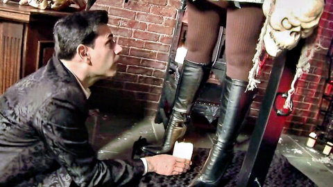 Man in suit kneels worshiping woman's legs in stockings and boots