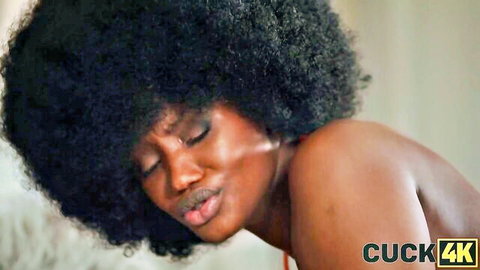 Seductive ebony babe with massive afro hair pouts topless showing bare shoulders and cleavage