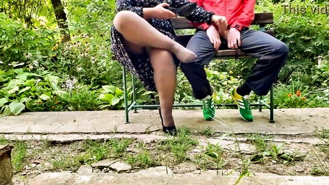 Woman in black dress and stockings crosses legs showing heels for cum fetish with man beside her