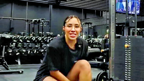 Fit black woman with braids squatting in gym t-shirt and shorts