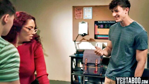 Redhead MILF teacher with glasses smiles at two young studs in classroom threesome setup