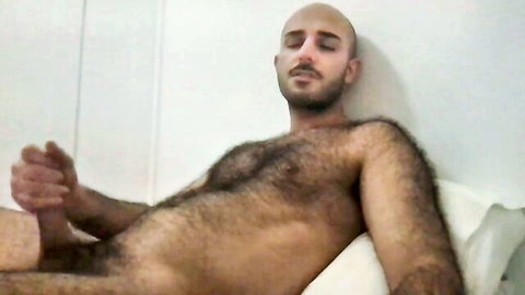 Hairy bald Arab man lying naked, exposing erect penis and body hair