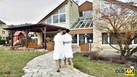 Older man and hot teen brunette couple in bathrobes walking outdoors