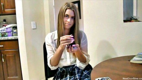 Skinny brunette teen schoolgirl in sheer blouse holding phone at kitchen table