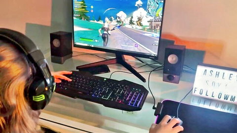Brunette gamer girl Ashley in headphones intensely playing Fortnite on PC