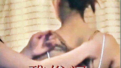 Chinese woman in thin strap top, hands gripping her back in bondage scene