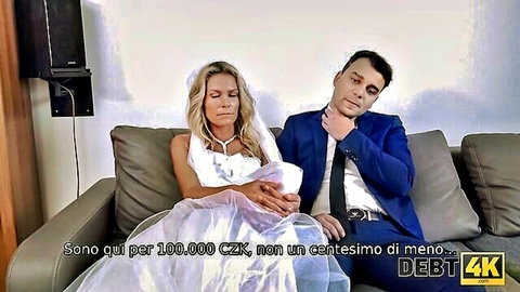 Blonde bride in white wedding dress sits with suited man on couch demanding 100000 CZK debt payment