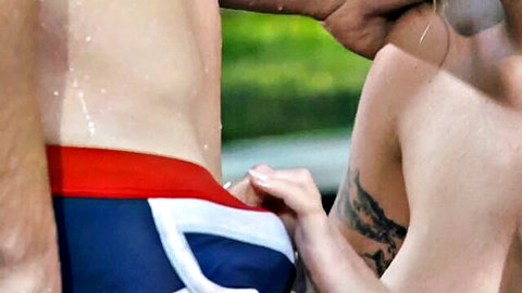 Woman's hand pulls down muscular man's tight speedo exposing his firm ass crack outdoors