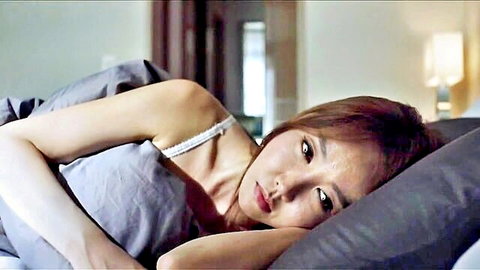 Sexy Korean babe lying seductively in bed wearing thin white camisole
