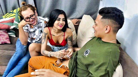 Busty tattooed brunette in red bra with redhead girlfriend and Latino stud smiling on couch