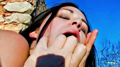 Brunette outdoor closeup with eyes shut as hand pries her mouth wide open
