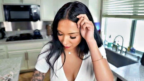 Sexy Asian mom with big tits in low-cut white top touching hair in kitchen