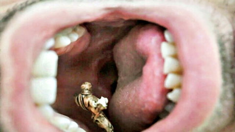 Tiny golden man figurine explores giant open mouth in macro fetish