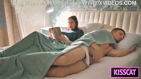 Brunette woman reads book on bed beside man with huge cock bulge in white underwear