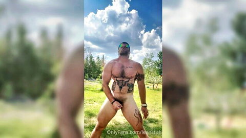 Muscular tattooed man nude outdoors, hand covering crotch in teasing pose