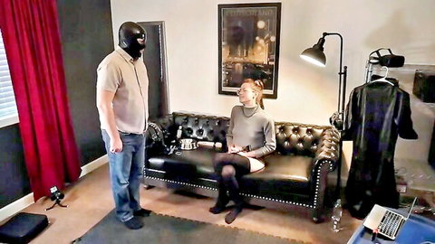 Miss Nina Paradisa trains masked beta boy in femdom session, smiling on couch