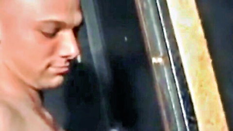 Bald muscular man staring at glory hole in arcade booth