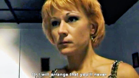 Intense blonde woman in revealing chainmail top, threatening glare in adult video thumbnail